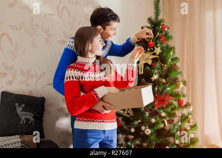 Paar in der Liebe schmücken Weihnachtsbaum mit Spielzeug zu Hause, tragen winter Pullover. Vorbereitung zum Neuen Jahr Stockfoto