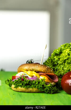 Leckerer cheesburger mit einer großen Anzahl von Gemüse, Senf, Mayonnaise, Salami und violette Zwiebel Ringe Stockfoto