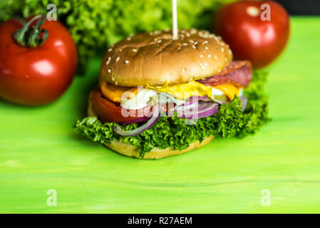 Leckerer cheesburger mit einer großen Anzahl von Gemüse, Senf, Mayonnaise, Salami und violette Zwiebel Ringe Stockfoto