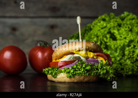 Leckerer cheesburger mit einer großen Anzahl von Gemüse, Senf, Mayonnaise, Salami und lila Zwiebelringe auf Holz, dunklen Hintergrund Stockfoto