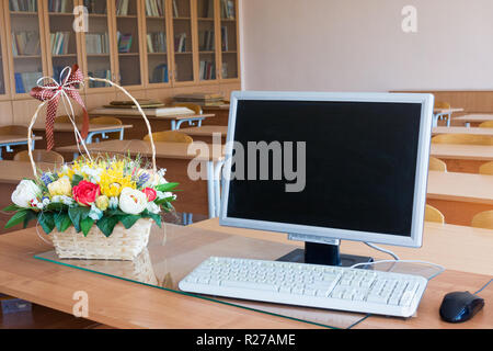 Korb mit Papier Blumen und Computer auf Lehrer Tabelle im Klassenzimmer Stockfoto