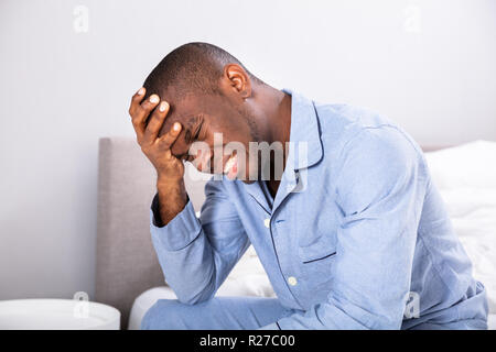 Seitenansicht eines jungen Mannes mit Kopfschmerzen sitzen auf dem Bett Stockfoto