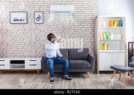 Junge afrikanische Mann Einschalten Klimaanlage mit Fernbedienung zu Hause Stockfoto