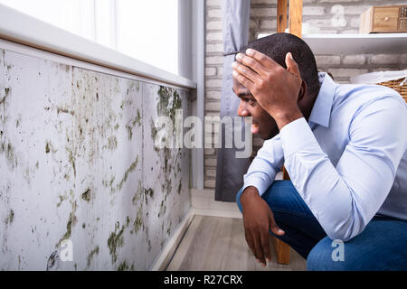 Seitenansicht eines Schockiert jungen afrikanischen Mann auf der Suche nach Schimmel an der Wand Stockfoto