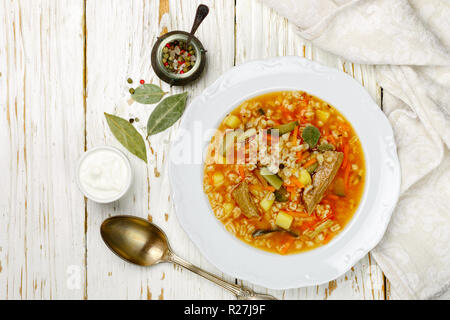 Traditionelle russische Suppe Rassolnik Rindfleisch mit eingelegten Gurken, Kartoffeln, Karotten, Zwiebeln, Tomaten, Graupen in Schale auf Holztisch. Ansicht von oben. C Stockfoto