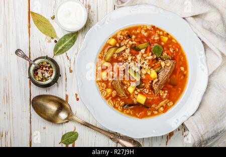 Traditionelle russische Suppe Rassolnik Rindfleisch mit eingelegten Gurken, Kartoffeln, Karotten, Zwiebeln, Tomaten, Graupen in Schale auf Holztisch. Ansicht von oben. C Stockfoto