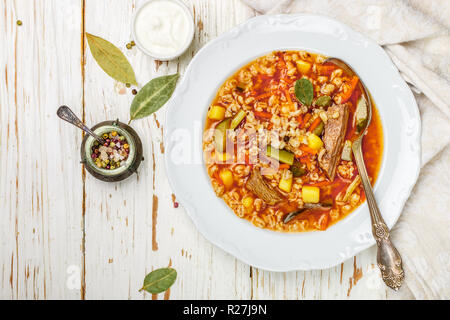 Traditionelle russische Suppe Rassolnik Rindfleisch mit eingelegten Gurken, Kartoffeln, Karotten, Zwiebeln, Tomaten, Graupen in Schale auf Holztisch. Ansicht von oben. C Stockfoto