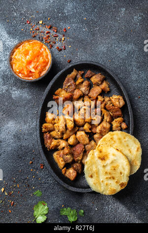 Kolumbianische essen. Gebratenes Schweinefleisch CHICHARRON, AREPAS und kolumbianischen Tomatensauce. Ansicht von oben. Schwarzer Hintergrund Stockfoto