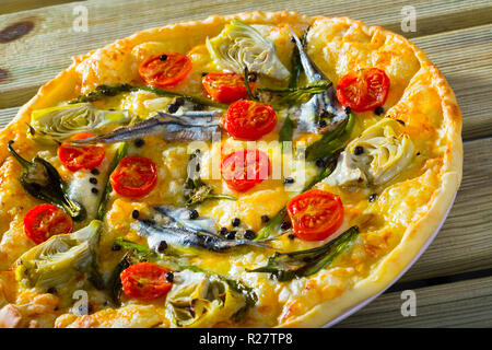 Italienische Pizza mit Sardellen, Artischocken, Käse und getrockneten Tomaten auf dünnem Teig ohne Hefe Stockfoto