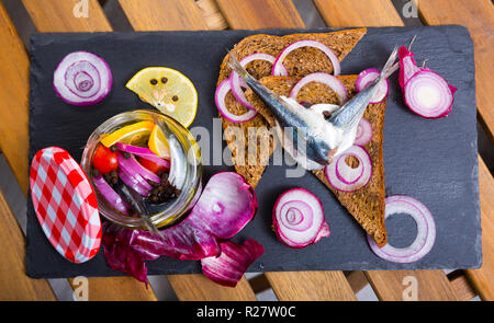 Gebeizt Sprotten in hausgemachten Marinade aus Olivenöl, Essig, Zitronensaft, Meersalz mit Gewürzen, Zwiebeln und Zuckerrüben mit Roggenbrot serviert. Stockfoto