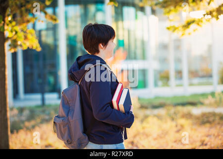 Seitenansicht im Freien Portrait von jungen Studenten Mädchen, dass zwei Bücher und Durchführung Rucksack gehen zur Hochschule, sonnigen Herbsttag. Stockfoto