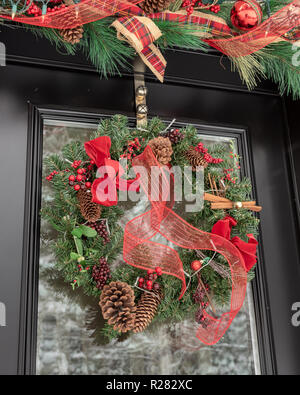 Traditionelle Weihnachten Kranz auf Tür mit verschneiten Hintergrund Reflexion hung Stockfoto