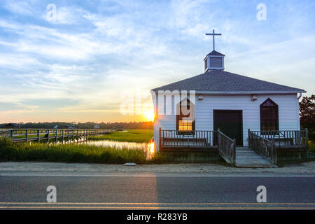 Kleine weiße hölzerne Kapelle auf dem Wasser an der Küste, während ein bunter Sommer Sonnenuntergang Stockfoto