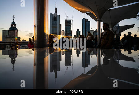 17. November 2018, Hessen, Frankfurt am Main: Frankfurter Skyline mit seiner Bank Towers ist im Abendlicht in einem Glas Oberfläche auf der Dachterrasse ein Restaurant im Zentrum der Stadt wider. Foto: Frank Rumpenhorst/dpa Stockfoto