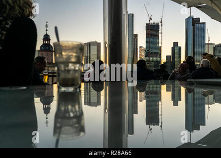 17. November 2018, Hessen, Frankfurt am Main: Frankfurter Skyline mit seiner Bank Towers ist im Abendlicht in einem Glas Oberfläche auf der Dachterrasse ein Restaurant im Zentrum der Stadt wider. Foto: Frank Rumpenhorst/dpa Stockfoto