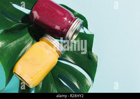 Lecker appetitlichen frischen Frucht Smoothies in Töpfen auf monstera Blatt auf blauen Tabelle. Sicht von oben mit kopieren. Tropischen Hintergrund. Stockfoto