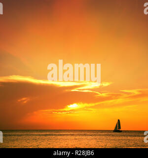 Orange Farbe marine Bild mit glänzenden Meer und Segelboot über bewölkten Himmel und Sonne bei Sonnenuntergang in Cozumel, Mexiko Stockfoto