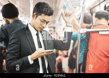 Junge und schöne asiatische Geschäftsmann mit Smartphone in einem pendlerzug. Konzept der Geschäftsleute und drahtlose Technologien Stockfoto