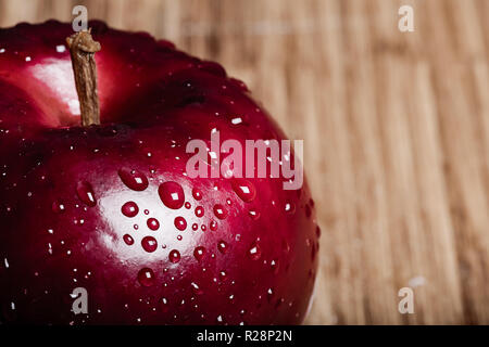 Ein roter Apfel mit Wassertropfen auf der Oberfläche. Viel Platz für Kopie auf der rechten Seite des Bildes über einen Bambus Schneidebrett. Stockfoto