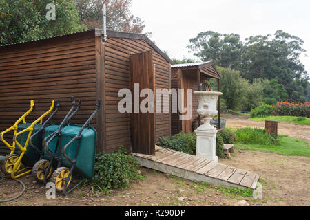 Schubkarren aufgereiht und Ruhen oder lehnte sich gegen Holz- gerätehaus oder Spielhaus im Freien Stockfoto