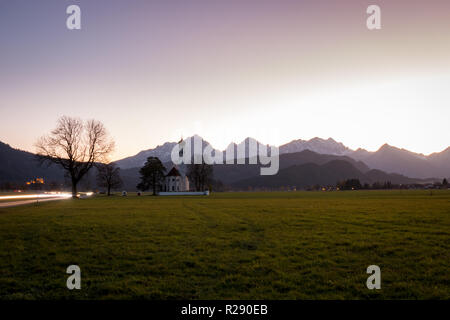 St. Coloman Kirche neben Schloss Neuschwanstein in Bayern, Deutschland in der Dämmerung mit bunten Himmel und Berge im Hintergrund Stockfoto