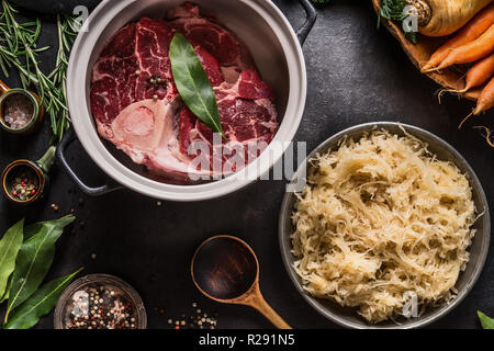 Zutaten für low carb Sauerkraut und Rindfleisch Eintopf oder Suppe. Rohes Rindfleisch Fleisch shin mit Knochen Kochtopf mit Gewürzen und Schüssel mit eingelegten Ca Stockfoto