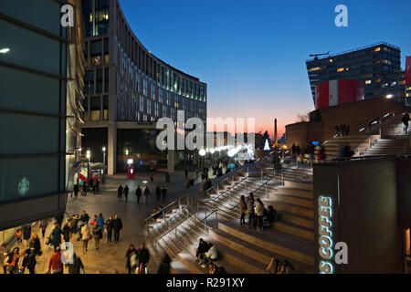 Menschen zu Fuß über Chavasse Park Liverpool UK in der Dämmerung, aus Liverpool ONE mit dem Hilton Hotel auf der linken Seite und Chavasse Schritte nach rechts. Stockfoto