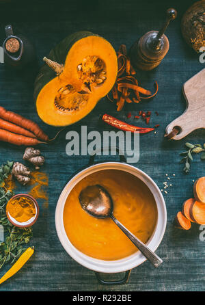 Kürbissuppe. Kochtopf am Küchentisch Hintergrund mit orange Gemüse und Gewürze Zutaten: Mit Orange kochen Zutaten: Kürbis, süß Stockfoto