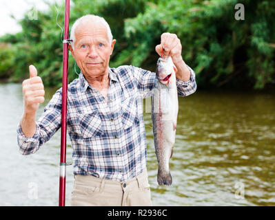 Senior kaukasischen Fischer mit Angeln große Forellen in der Hand zufrieden Stockfoto