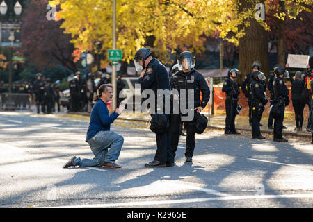 Portland, OR/USA, 17. November 2018: Demonstrator in der Innenstadt von Portland auf seinen Knien in der Mitte der Straße. Zwei Polizisten versuchen, Grund Stockfoto