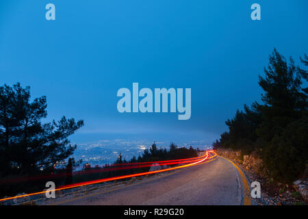 Auto Lampen auf dem Berg während der Blauen Stunde, an einem kalten Wintertag, in Berg Hymettus, in Athen, Griechenland. Stockfoto