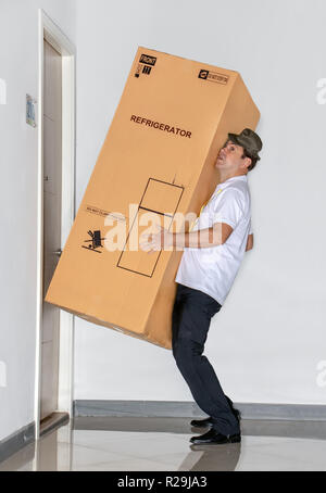 Der Postbote trägt ein grosses Paket mit Kühlschrank. Der E-Mail-Dienst trägt einen großen Sendung mit einem Kühlschrank in die Wohnung. Stockfoto