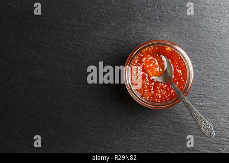 Roter Kaviar in einem Glas mit einem Löffel auf einem schwarzen Hintergrund. Platz für Text Stockfoto