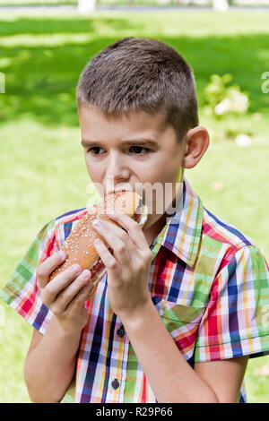 Süße brünette Junge essen Hotdog mit Appetit Stockfoto