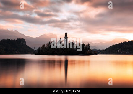 Bunte sunrise Blick auf See von Bled in den Julischen Alpen, Slowenien. Wallfahrtskirche der Himmelfahrt der Maria im Vordergrund. Landschaftsfotografie Stockfoto