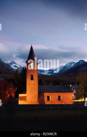 Christentum Kirche Sils Dorf (in der Nähe von See Sils) in den Schweizer Alpen. Orangefarbenes Licht auf Gebäude und die schneebedeckten Berge im Hintergrund. Schweiz Stockfoto