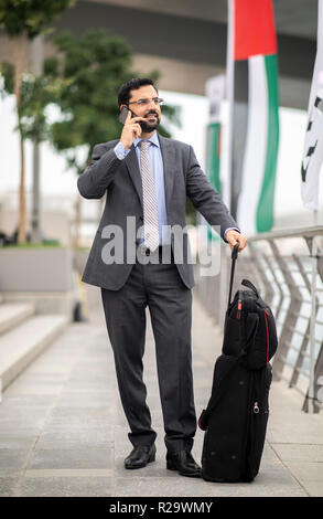 Arabische Geschäftsmann mit seinem Koffer in einer Stadt, die auf einem Telefon Stockfoto