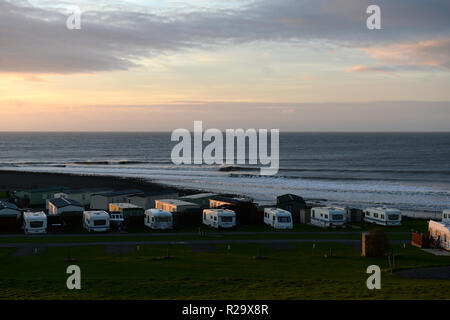 Llanrhystud Strand bei Sonnenuntergang Licht über der Flussmündung brechen und Kiesel Shoreline mit mehreren Wohnwagen im Vordergrund suchen Stockfoto