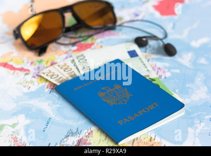 Ukrainische Reisepass auf einer Weltkarte. Euro-banknoten, Portemonnaie, sunglasees und Ohrhörer im Hintergrund. Stockfoto