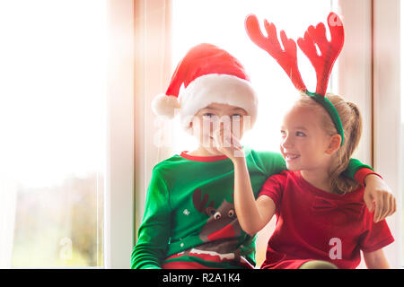 Bruder und Schwester auf der Fensterbank an Weihnachten sitzen, gemeinsam Spaß zu haben. Weihnachten Familie Zeit Lebensstil. Stockfoto