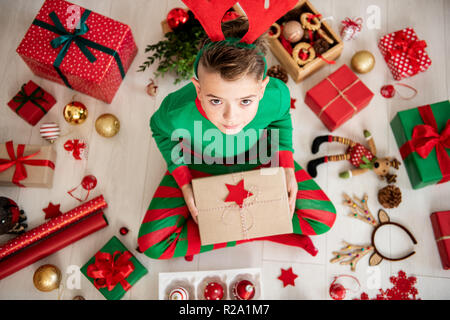 Neugierige Junge tragen xmas Schlafanzug sitzen auf dem Boden und öffnete seine Weihnachtsgeschenk, Ansicht von oben. Stockfoto