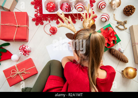 Süße Mädchen schreiben Brief an Santa auf Wohnzimmer Erdgeschoss. Überblick über ein junges Mädchen, das ihr Weihnachten Wunschzettel schreiben. Stockfoto