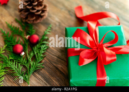 DIY Geschenkverpackung. Wunderschöne grüne Weihnachten Geschenke mit roter Schleife auf rustikalen Holztisch. Blick von oben auf die Weihnachten folierstation. Stockfoto