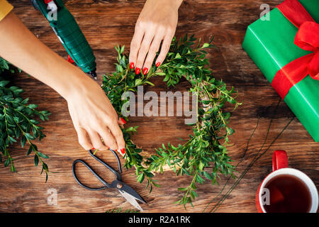 Frau unkenntlich machen Weihnachten Kranz. DIY Weihnachten Dekoration Konzept. Hände, Nahaufnahme, Ansicht von oben. Stockfoto