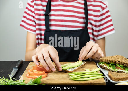 Die rohe Nahrung Sandwich. Weibliche Hände Scheiben Avocado auf Brot Stockfoto