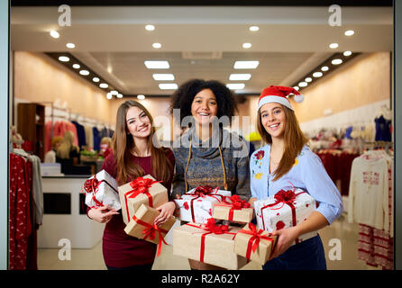 Drei gemischte Rennen Frauen mit geschenkboxen in Händen zu speichern. Multi-ethnische Mädchen lächelnd mit Geschenken zu Weihnachten neues Jahr verkaufen. Kaukasische und afrikanische amerikanische Frauen Shopping Geschenke für die Feiertage. Stockfoto