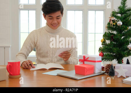 Mann mit Creme Pullover schreiben Weihnachten schreiben Grußkarte Urlaub wünsche mit Weihnachten Dekoration. Stockfoto