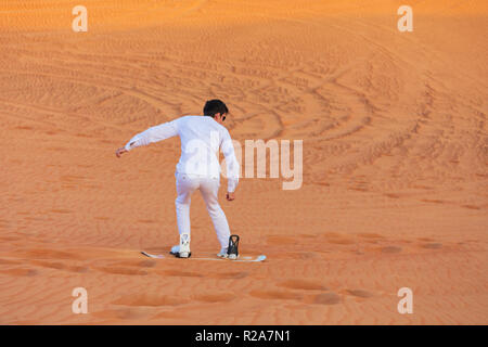 Junge touristische Mann in Weiß gekleidet, Kleidung Sand Boarding die Düne in einer Wüste in der Nähe von Dubai, VAE Stockfoto