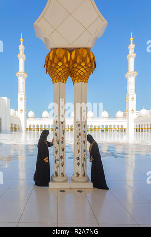 2 arabische Frauen tragen traditionelle schwarze Abaya während in der Sheikh Zayed Moschee in Abu Dhabi, Vereinigte Arabische Emirate mit Minaretten im Hintergrund beten Stockfoto