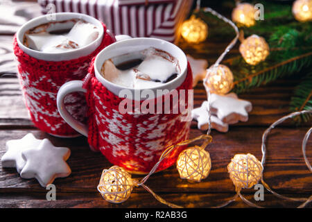 Heiße Schokolade mit Marshmallows und Keksen auf Weihnachtsschmuck Hintergrund. Garland und Tanne gemütliche Atmosphäre schaffen. Stockfoto